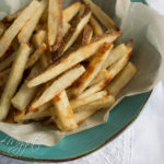 Crispy Baked French Fries on parchment paper on rustic teal bowl