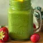 green smoothie in mason jar topped with strawberries and mango