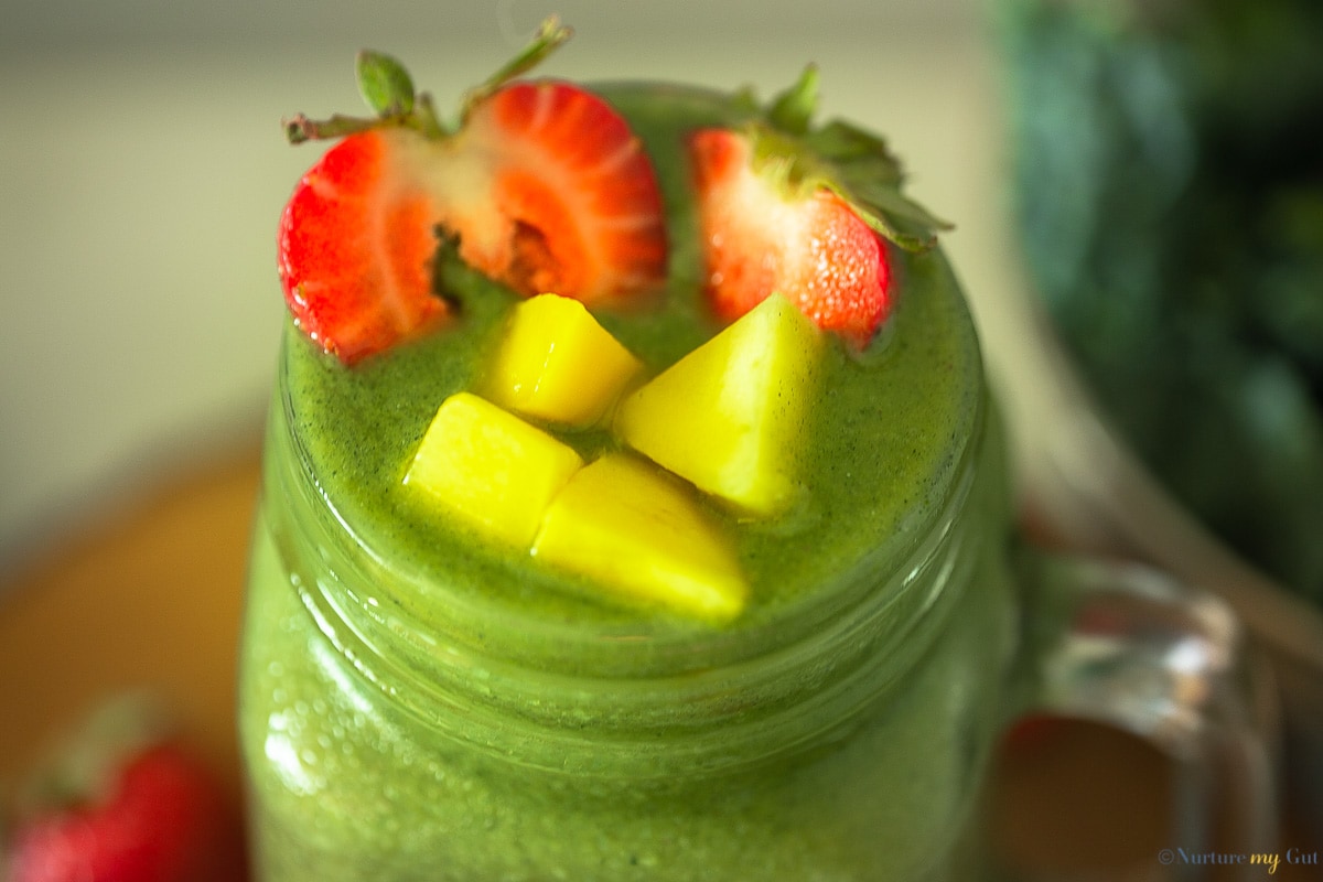 green smoothie topped with chopped mango and strawberries