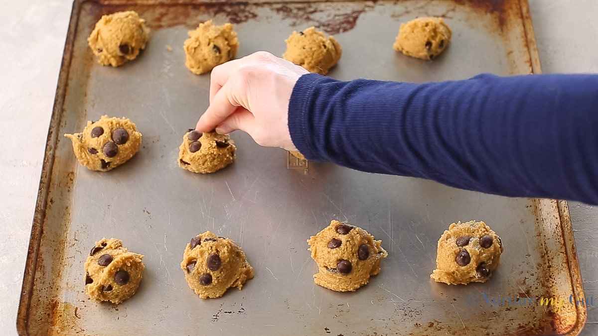 hand placing chocolate chips on cookie mounds on cookie sheet