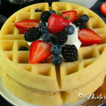 gluten free waffle on a white plate topped with whipped cream and fresh berries