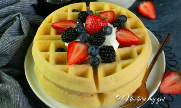 gluten free waffle on a white plate topped with whipped cream and fresh berries