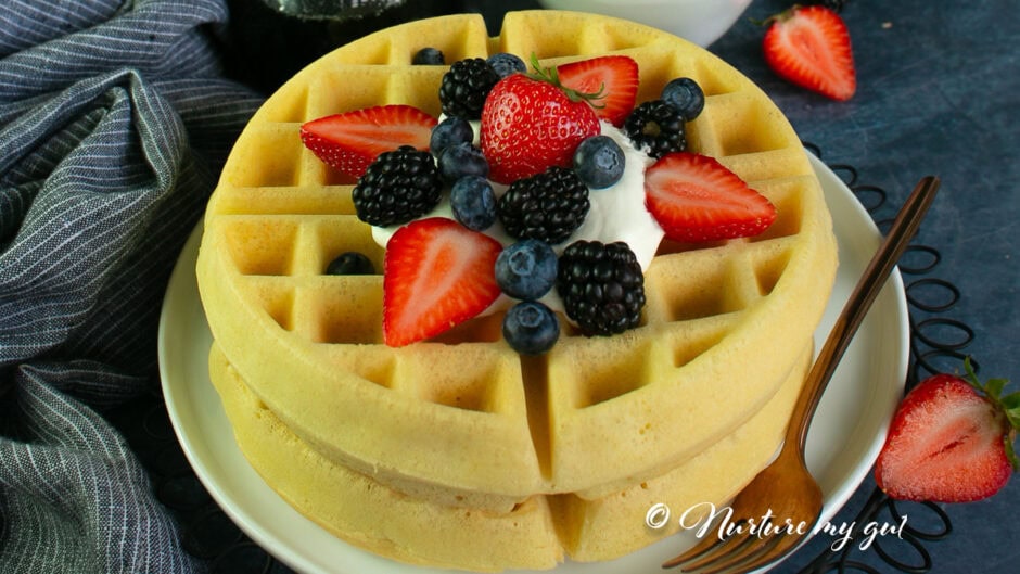 gluten free waffle on a white plate topped with whipped cream and fresh berries